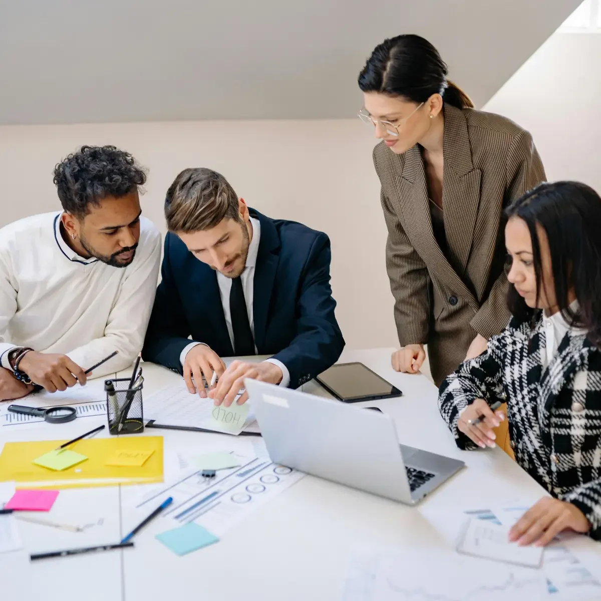 A group of professionals collaborates around a table filled with charts, sticky notes, and a laptop, engaged in a discussion.
